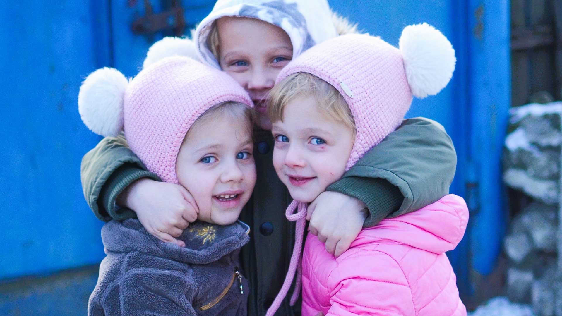 Three children in new warm clothes stand in the snow.