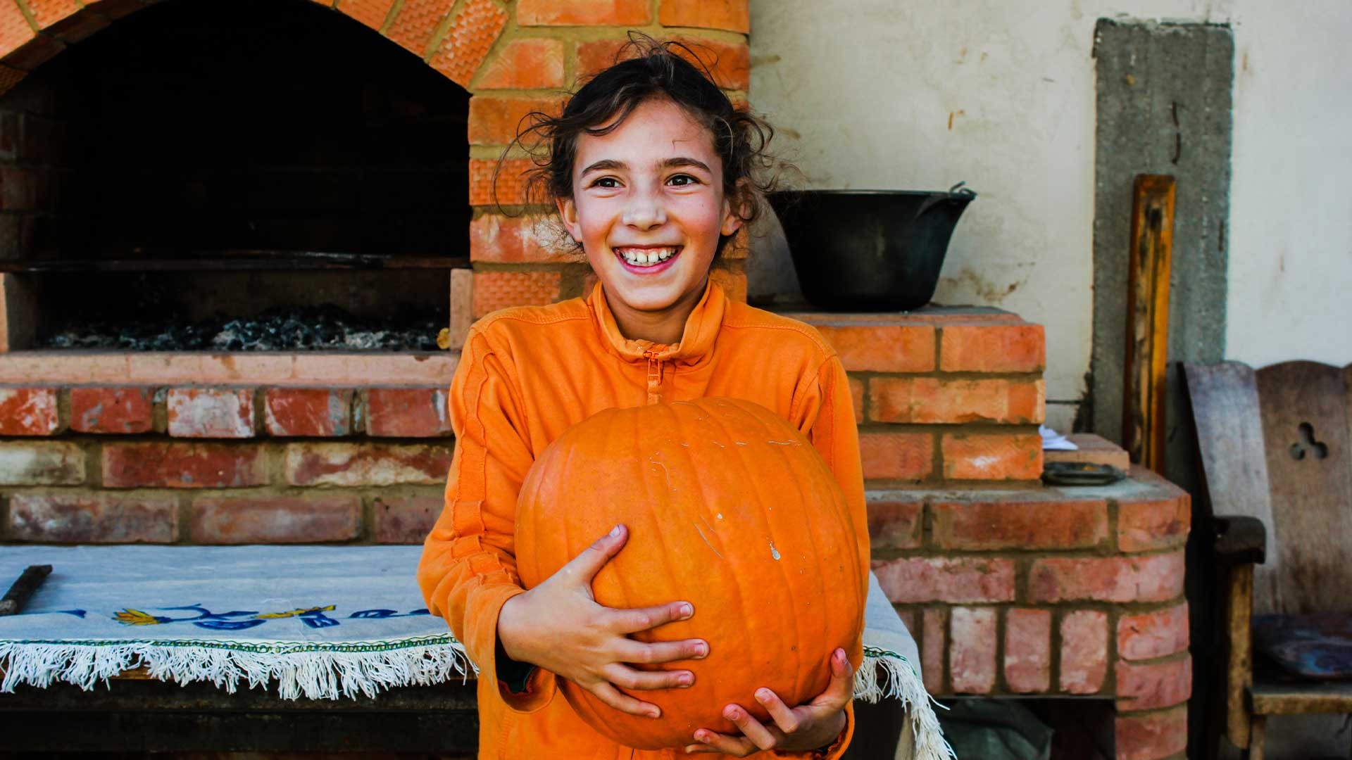 A child stands smiling with a pumpkin.