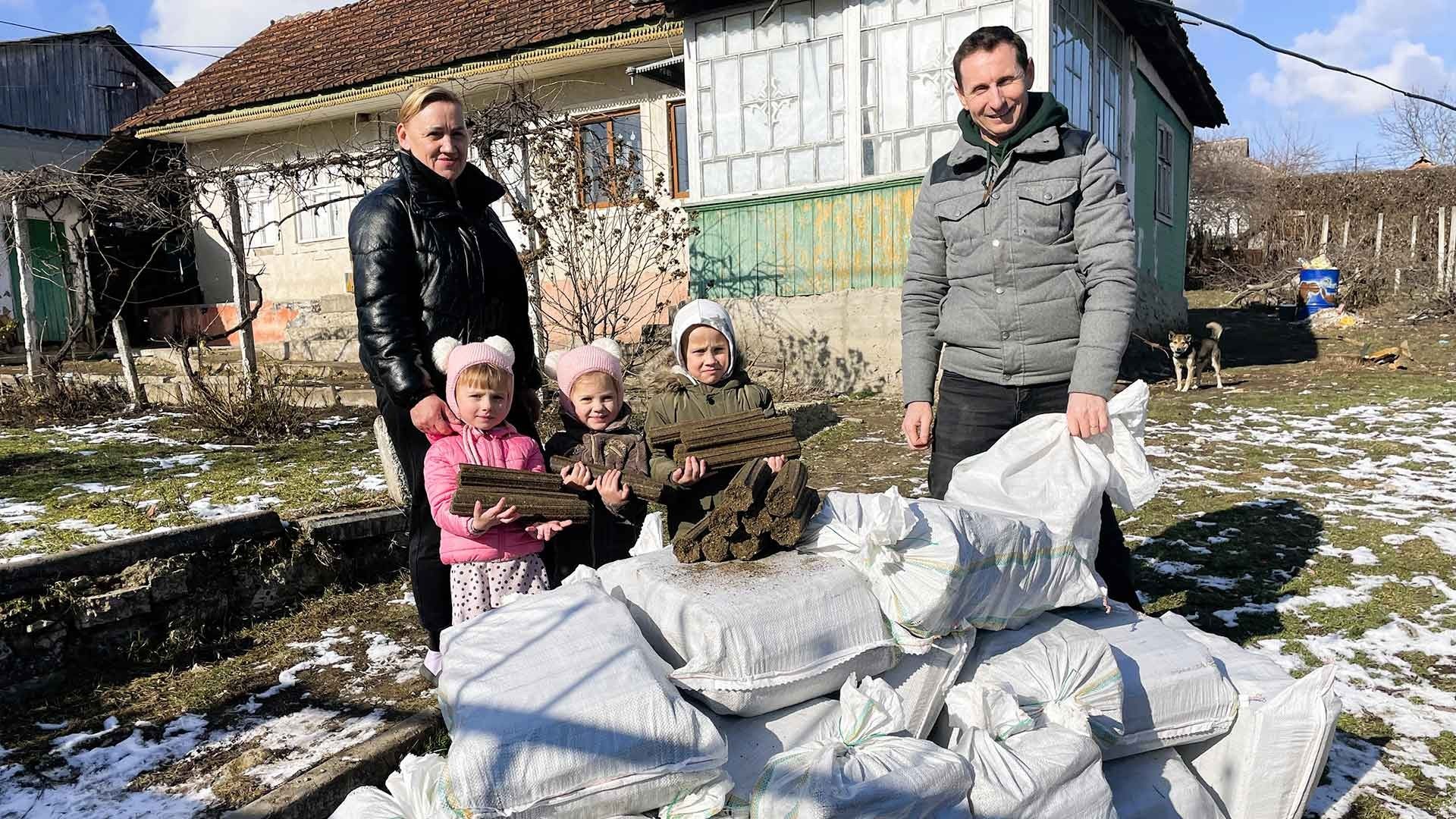 Family of five smile beside bags filled with firewood.