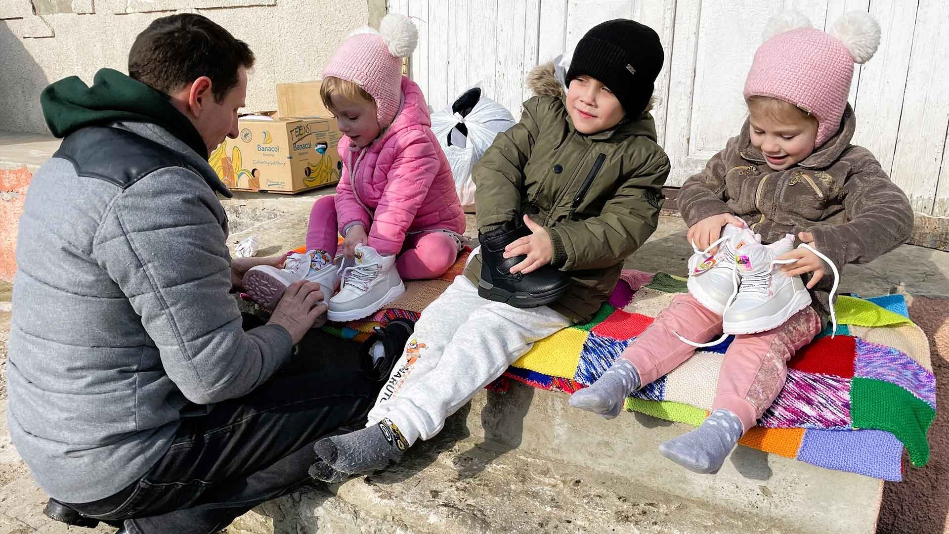 Father helps children on a knitted blanket try on their new shoes.